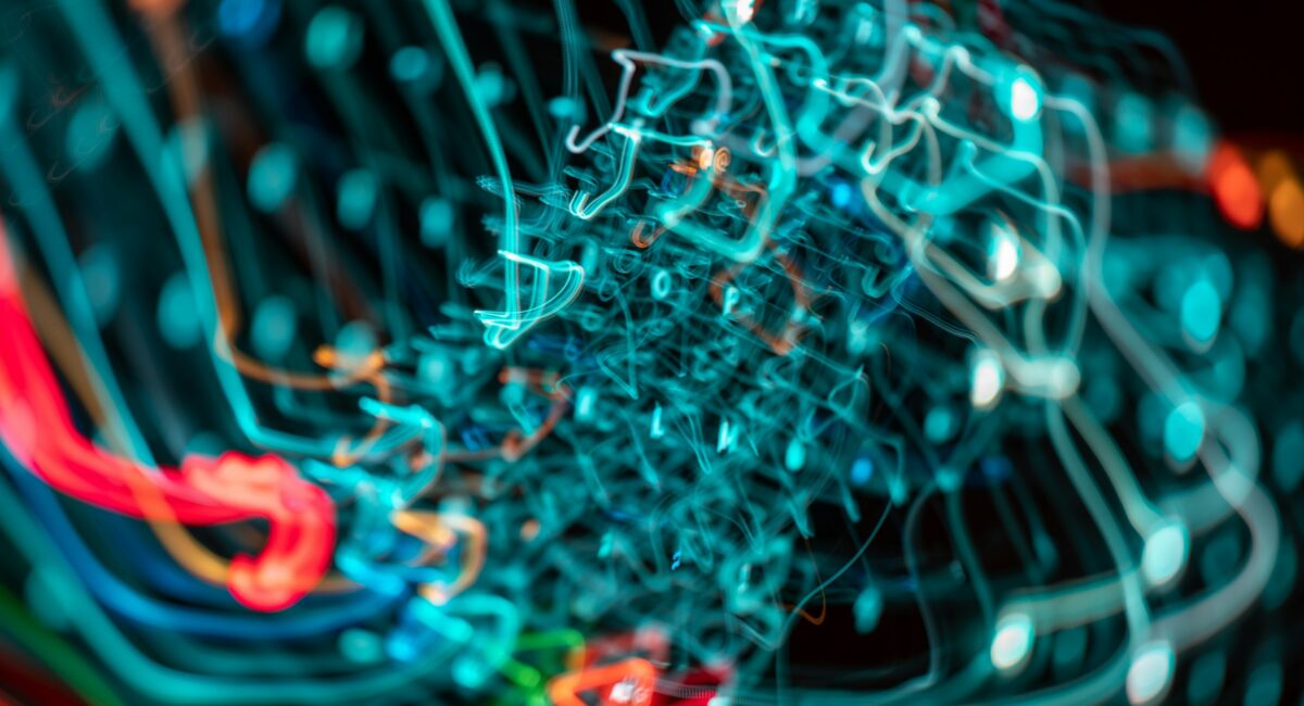 Abstract long-exposure photo of glowing teal, red, orange, and green light trails swirling together, evoking a tangled network of data connections